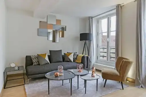 Salon d’un appartement meublé moderne avec canapé gris, fauteuil vintage et tables basses - Location pour professionnels en mobilité à Paris
